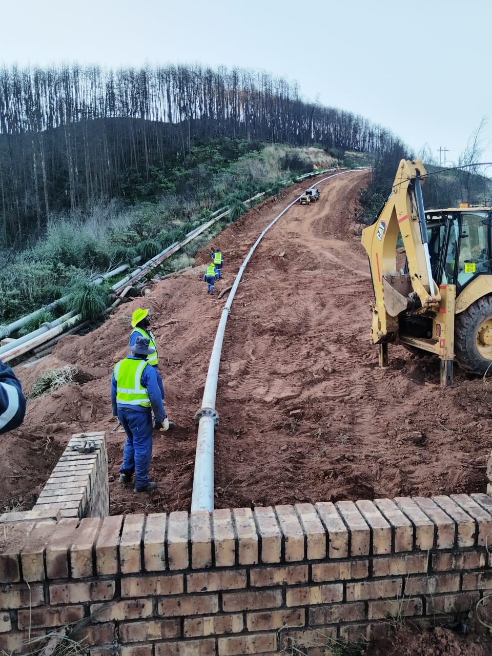 Wetpipe crew constructing an overland slurry pipeline along a hillside access track